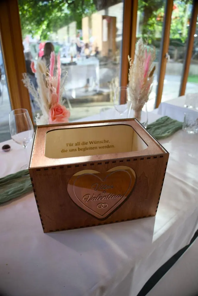 Kartenbox aus Holz mit Spiegelherz in Rosegold und graviertem Spruch innen, auf einem gedeckten Hochzeitstisch