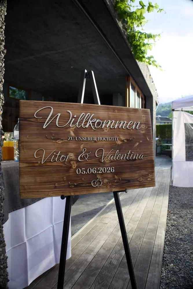 Willkommensschild aus geflammtem Holz auf einer Staffelei vor dem Eingang einer Hochzeitslocation