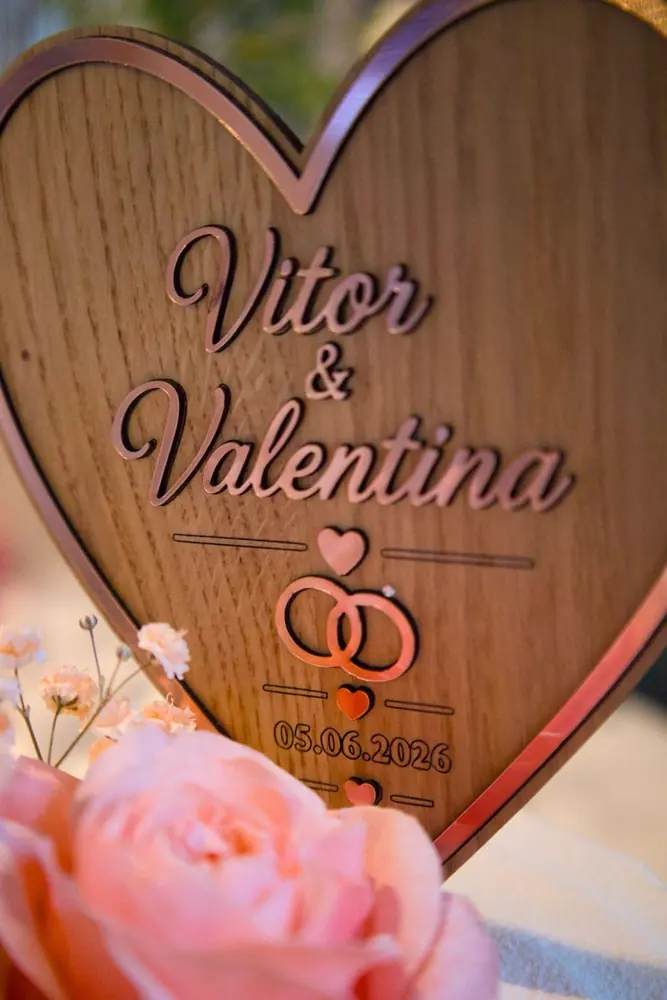Tortenstecker in Herzform aus Holz mit Namen, Ringen und Datum in Rosegold, davor eine Rose